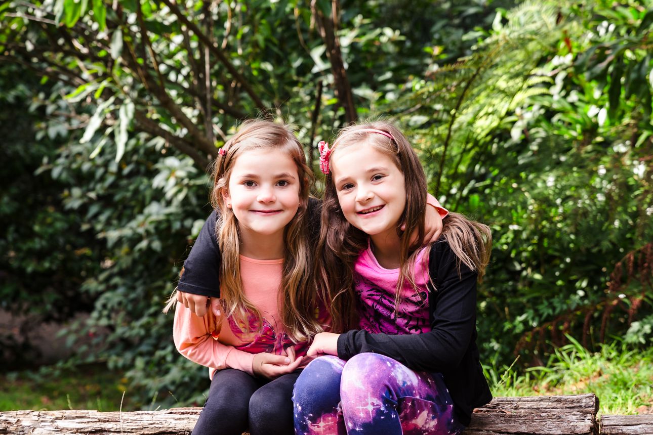 sisters sitting on a log at home during family photo session