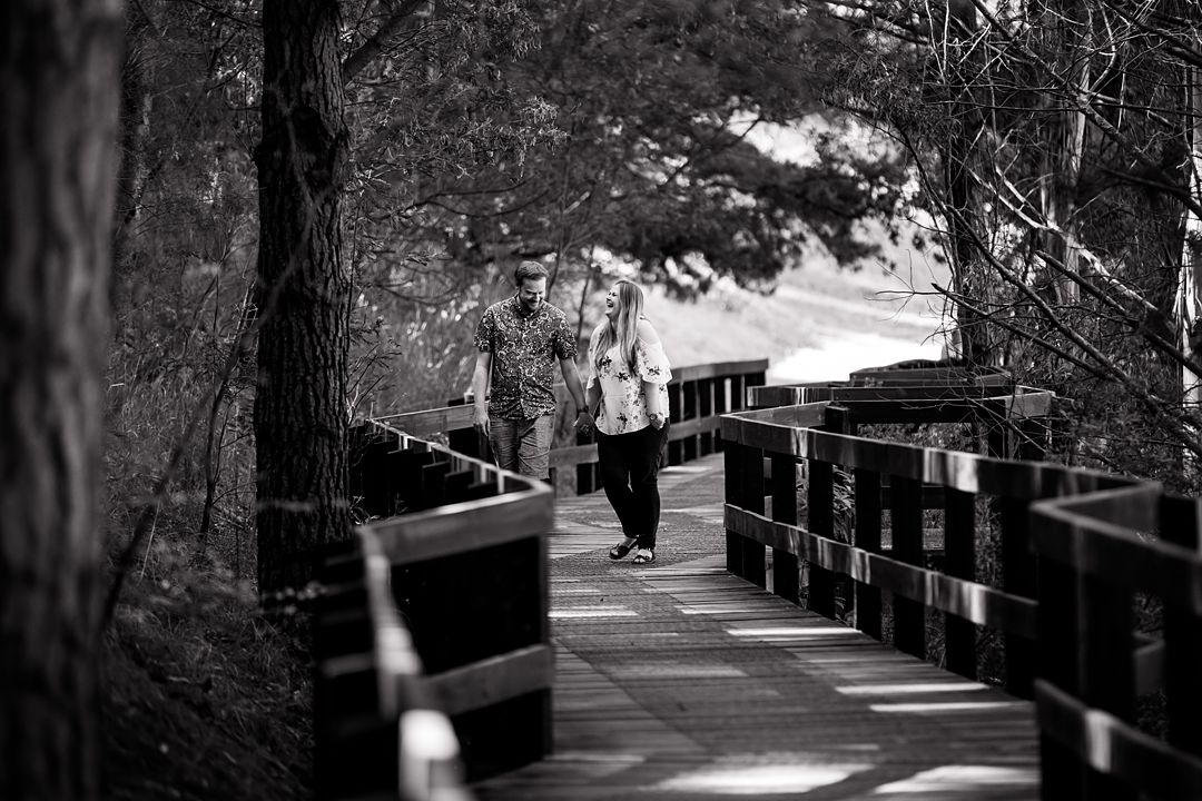 couple holding hands walking on the wooden bridge in Wilson botanic park during engagement photo session