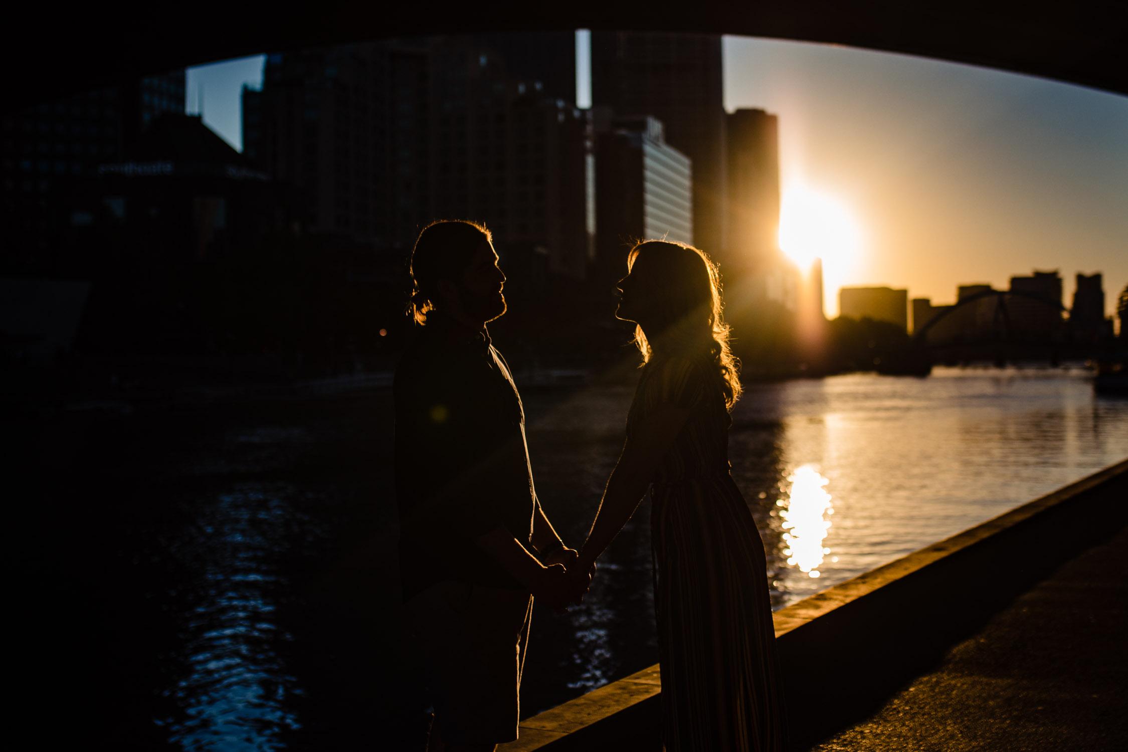 couple holding hands with the setting sun behind the Melbourne skyline behind them