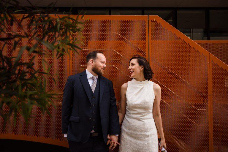 bride and groom holding hands in front of orange wall during abbotsford elopement