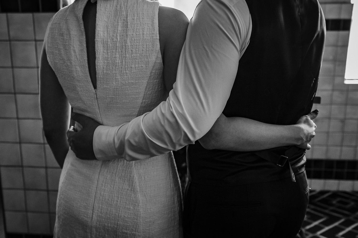 black and white image of bride and groom hugging from behind