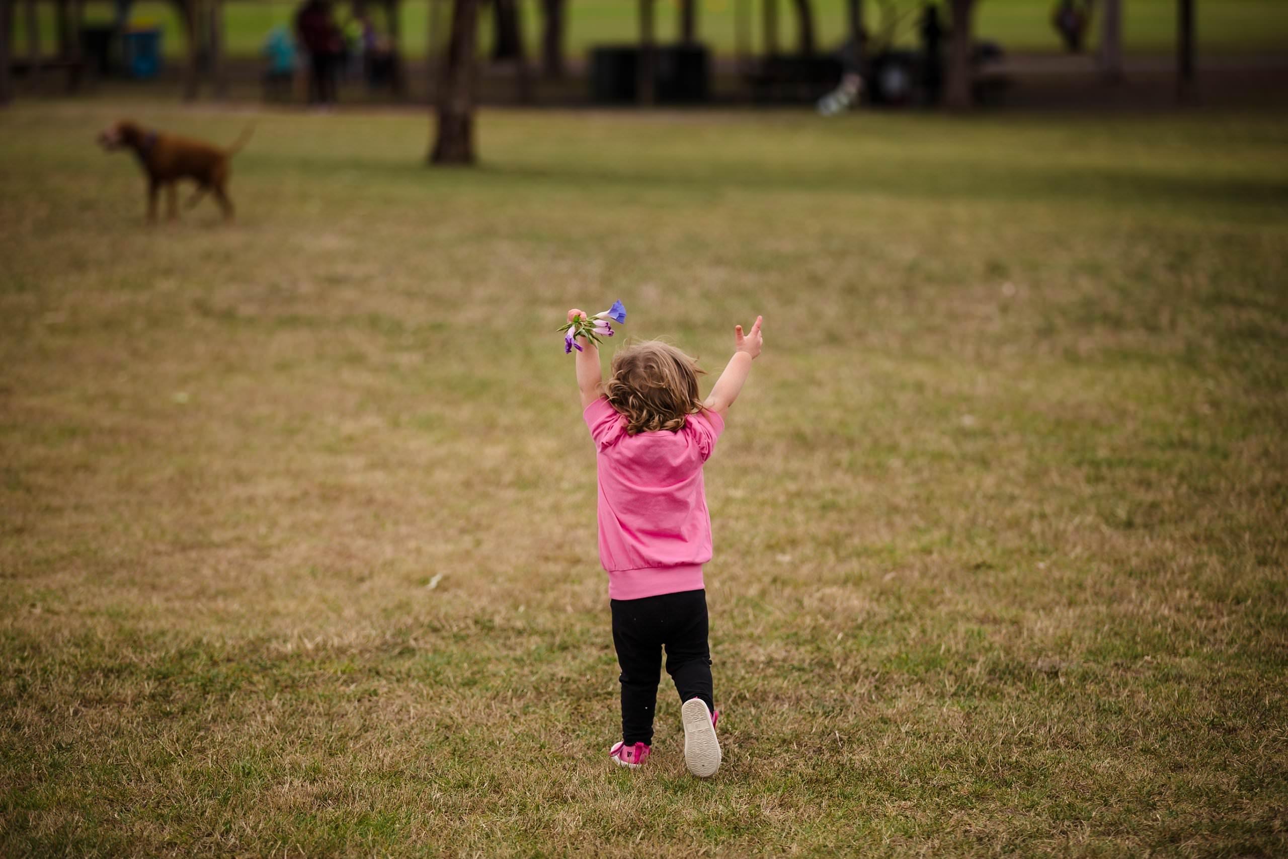 brighton maternity photographer captures toddler running through the park with hands in the air