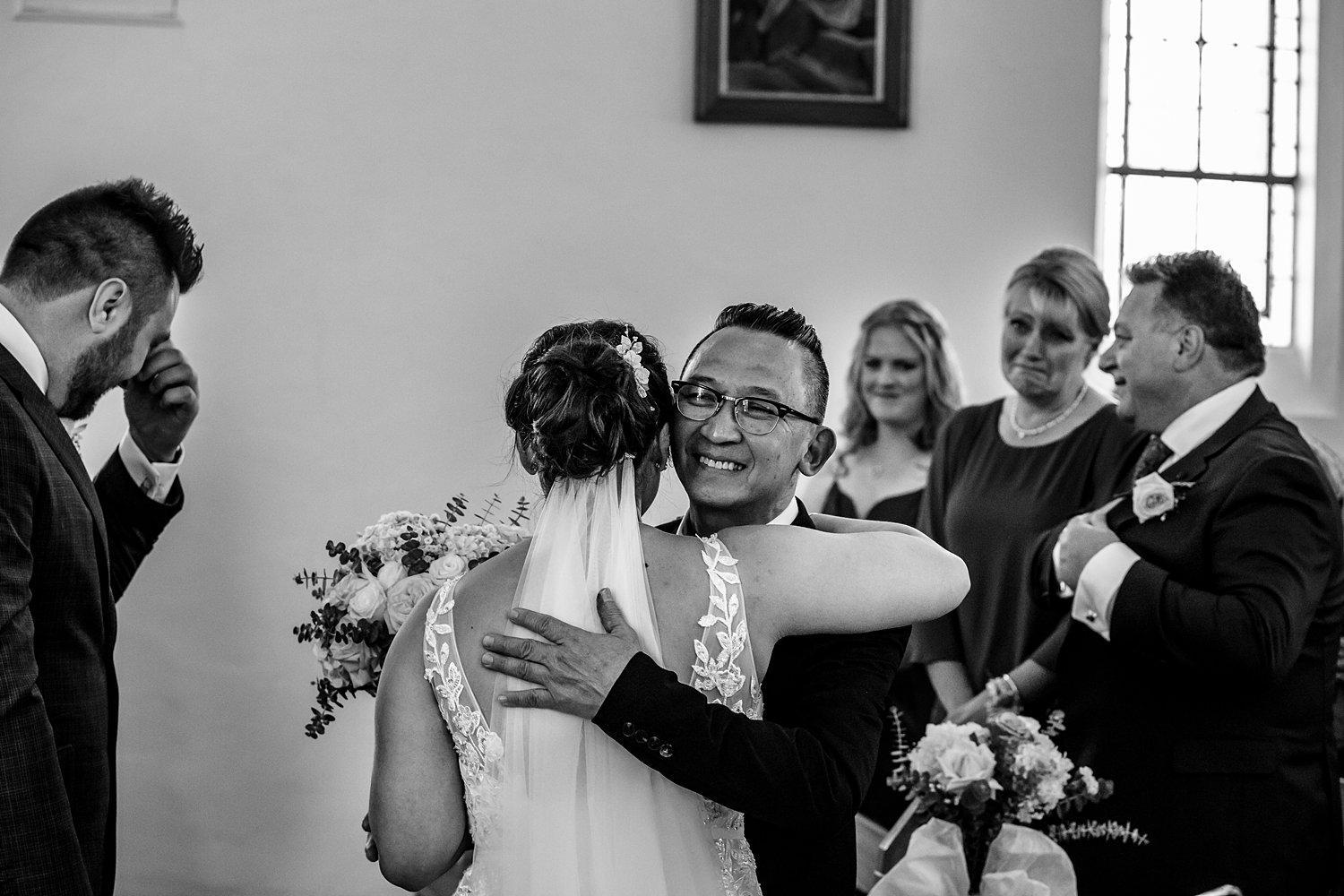 groom wipes tears as father of the bride hugs his daughter