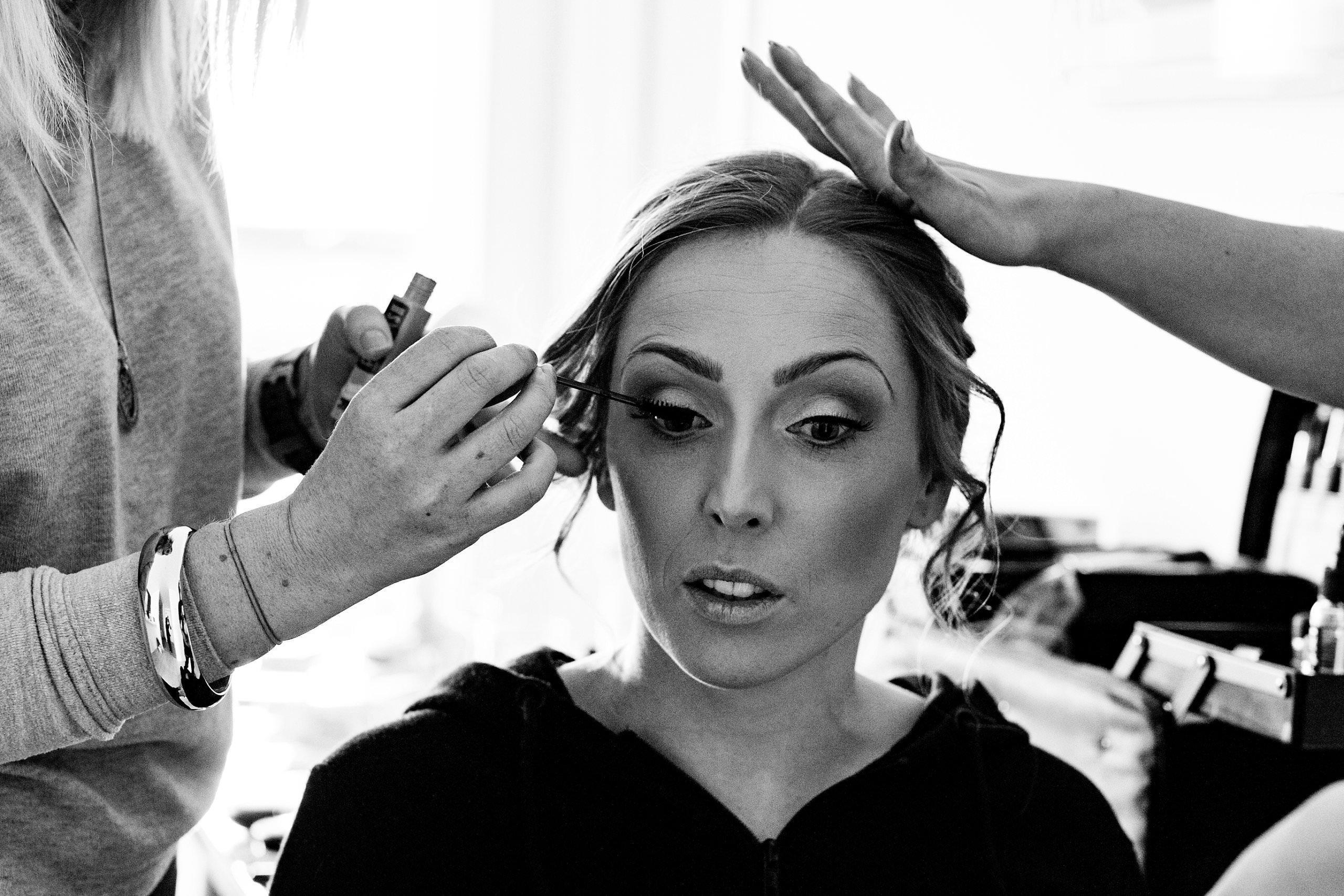 the make up artist putting mascara on the bride 
