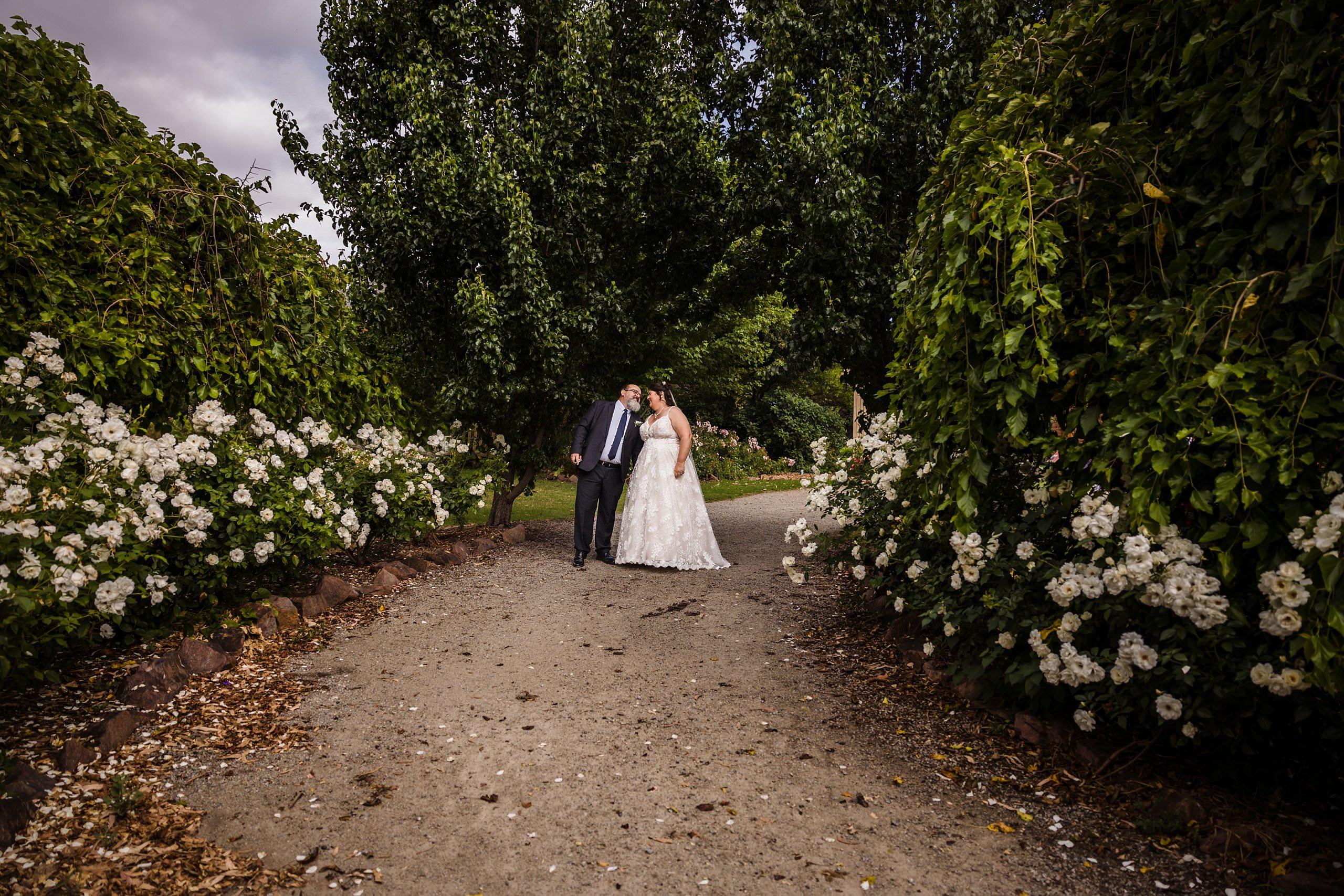 The Bride and Groom holding hands and walking through the rose garden at the old cheese factory