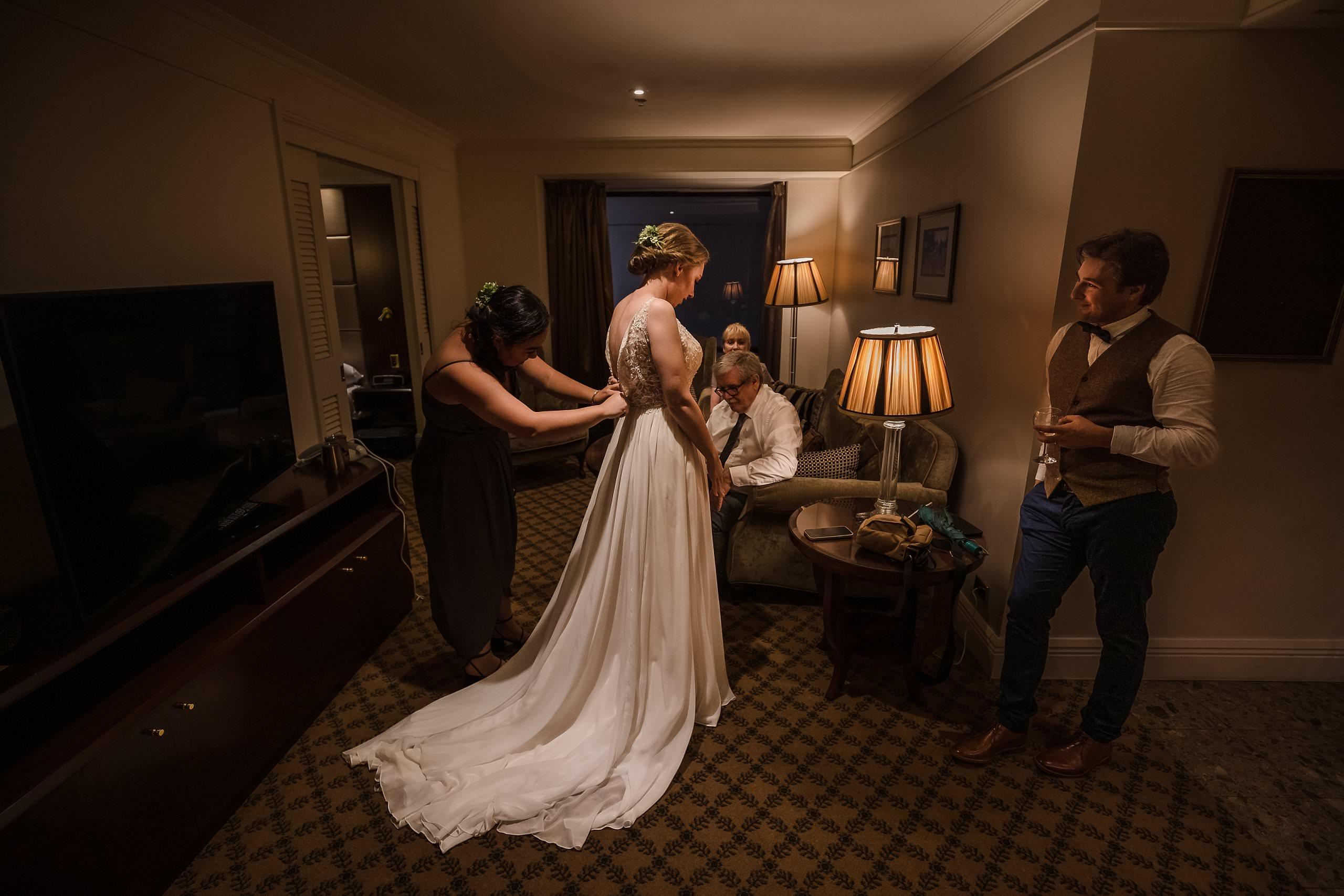 bride getting help puting on her wedding dress with her parents watch on