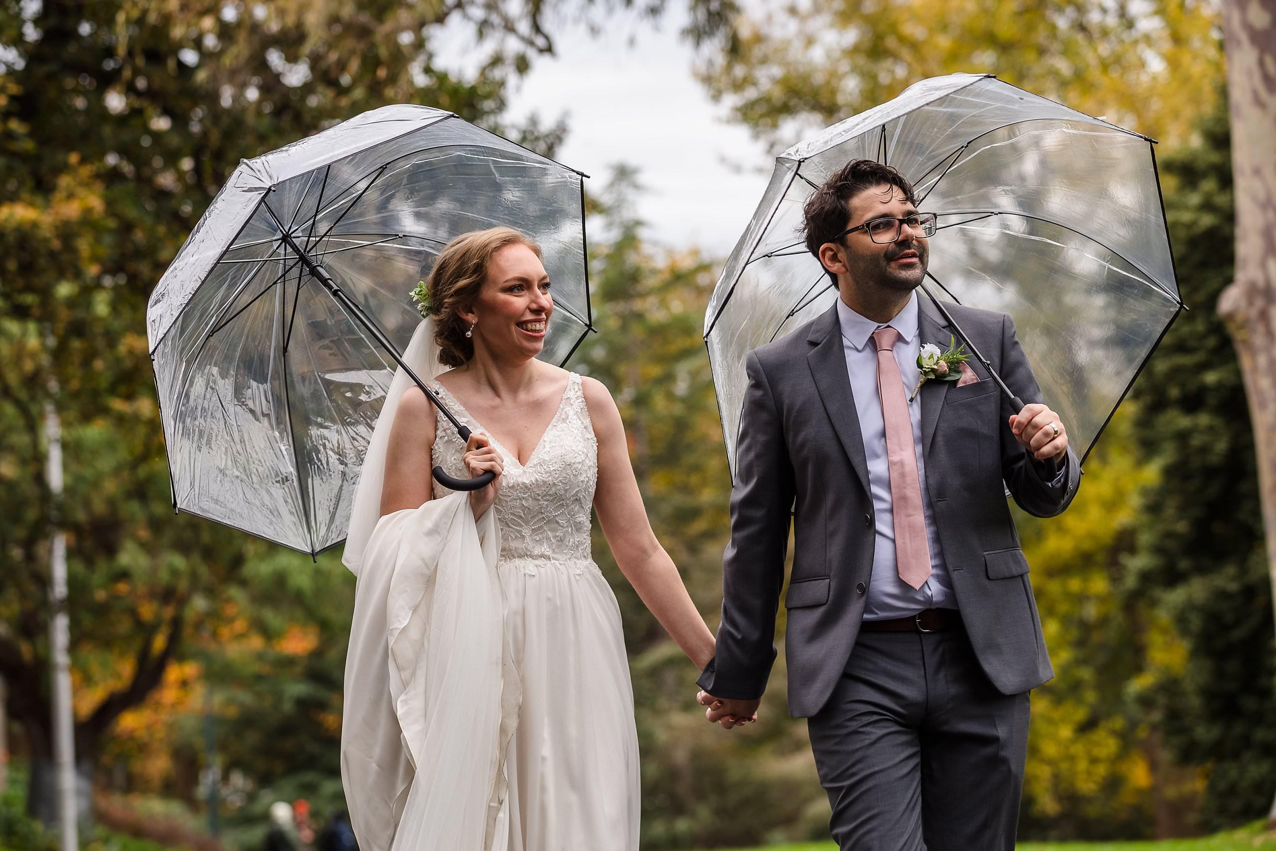 bride and groom walking and holding umbrellas