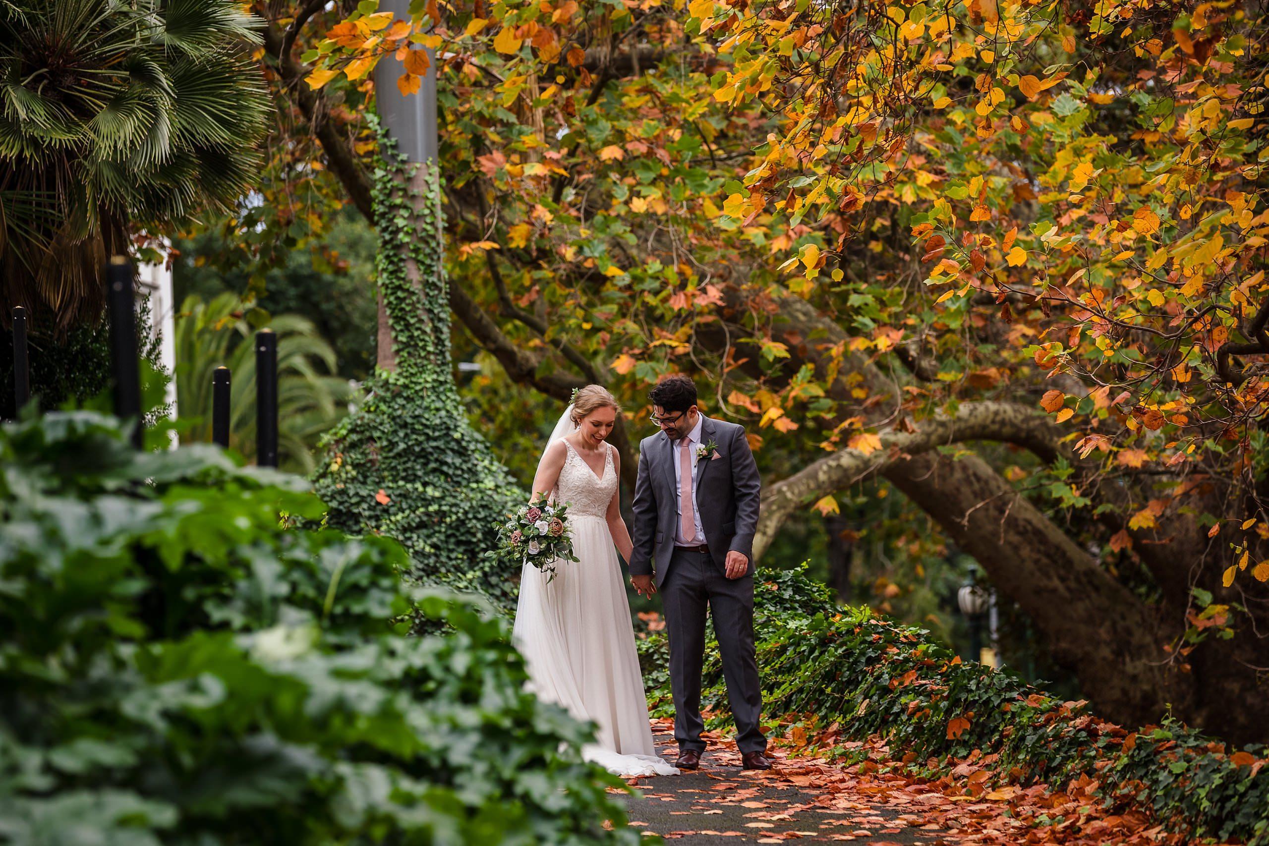 bride and groom holding hands in the treasury gardens with autumn leaves everywhere