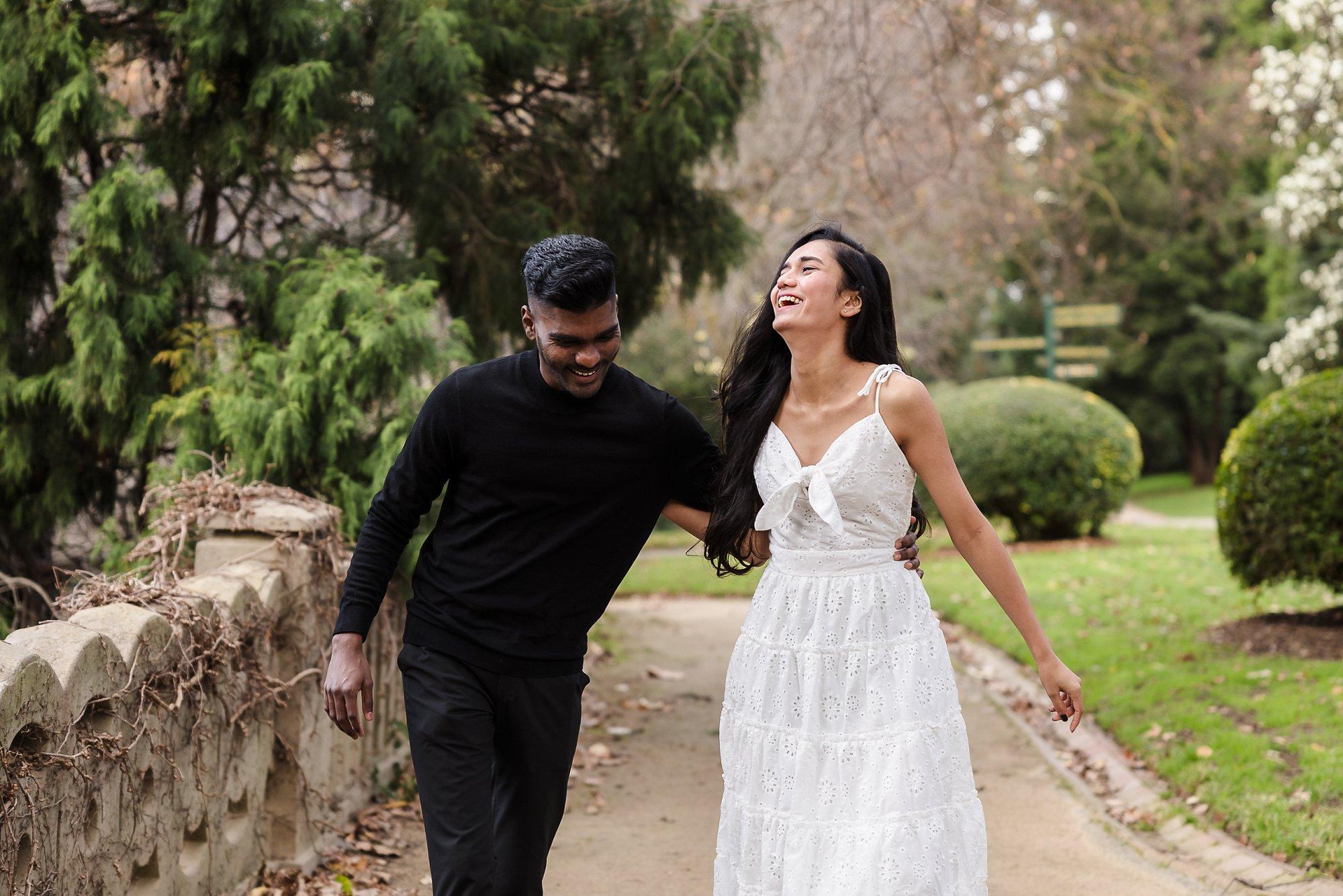recently engaged couple laughing and walkin in the Kings Domain gardens